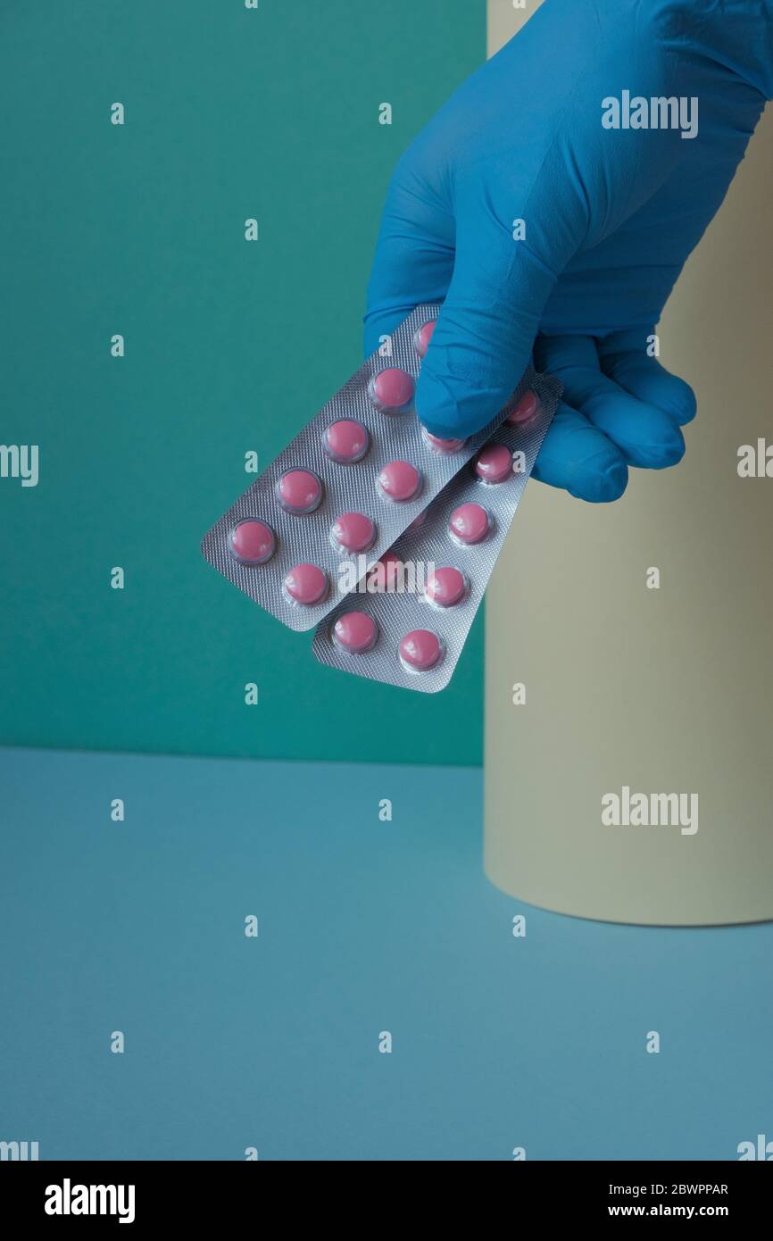 Concept de santé et de médecine. Traitement avec des pilules. Pilules roses dans un gant bleu sur fond vert-jaune.traitement de la maladie virale Banque D'Images