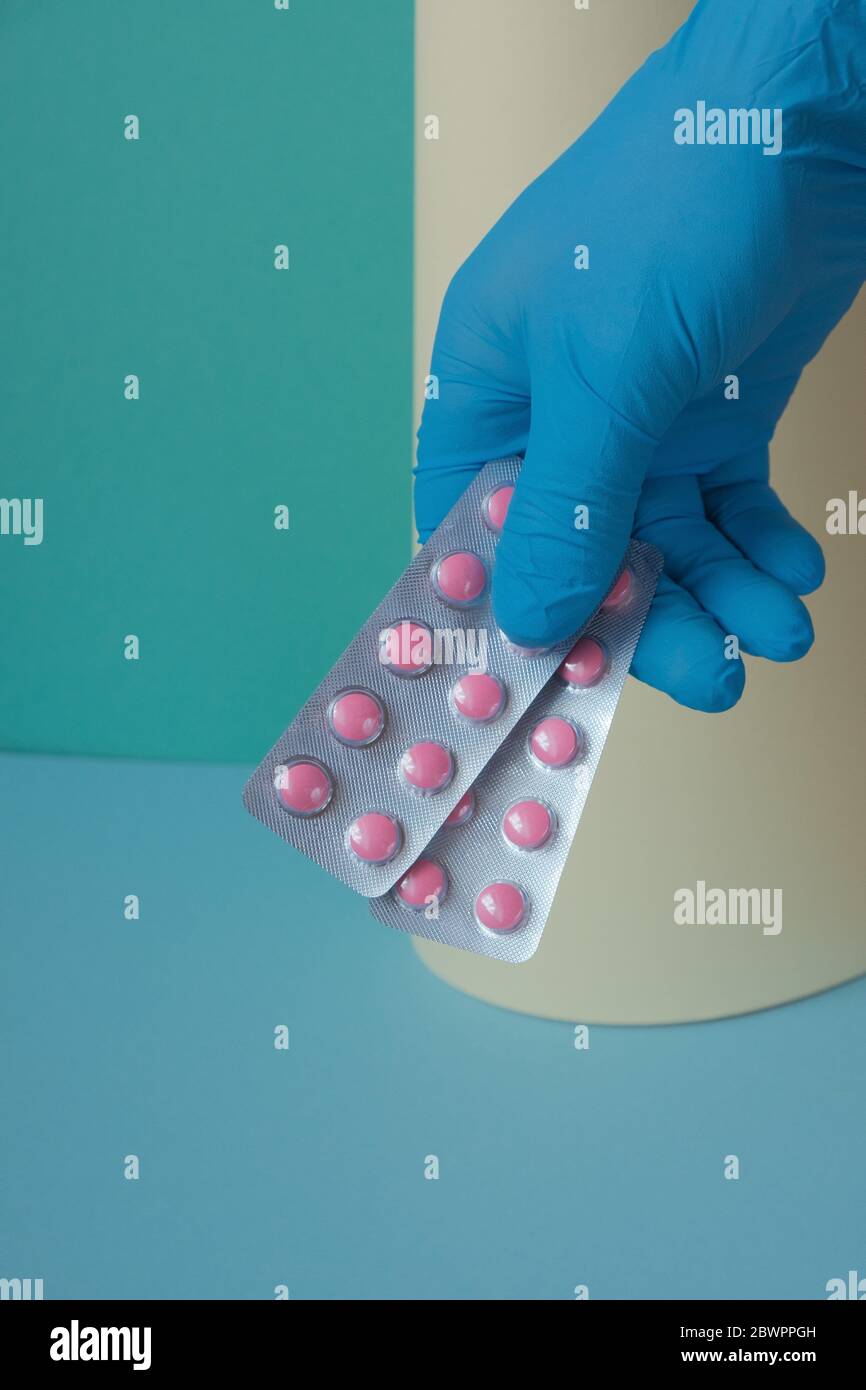 Santé et médecine . Traitement avec des pilules. Pilules roses en main dans un gant bleu sur fond vert-jaune.traitement de la maladie virale Banque D'Images