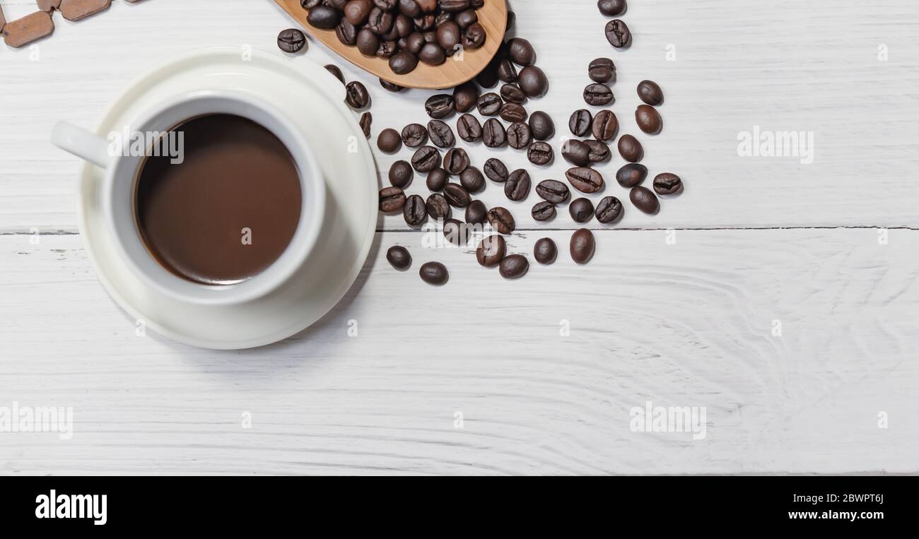 Tasse de café noir et grains de café de bons essentiels sur fond de bois blanc. Vue de dessus. Banque D'Images