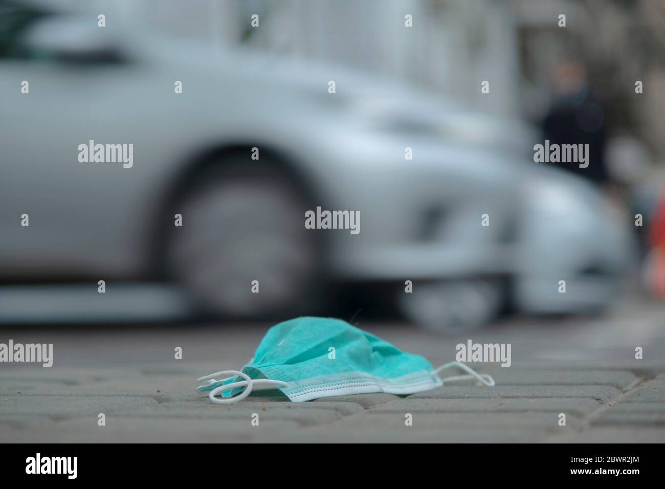 Le masque médical jeté se trouve sur le trottoir et les voitures conduisent en arrière-plan. Masques de visage polluant les rues de la ville depuis le coronavirus COVID-19. Mise au point douce. Banque D'Images