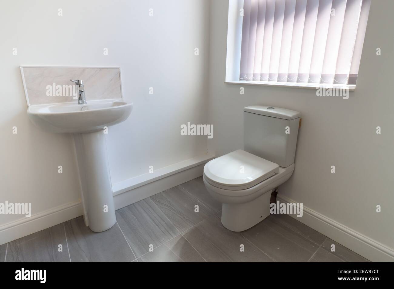 Photo d'une salle de bains britannique moderne et flambant neuve montrant  un lavabo et des toilettes récemment installés, avec sol carrelé gris, murs  blancs et plinthes W Photo Stock - Alamy