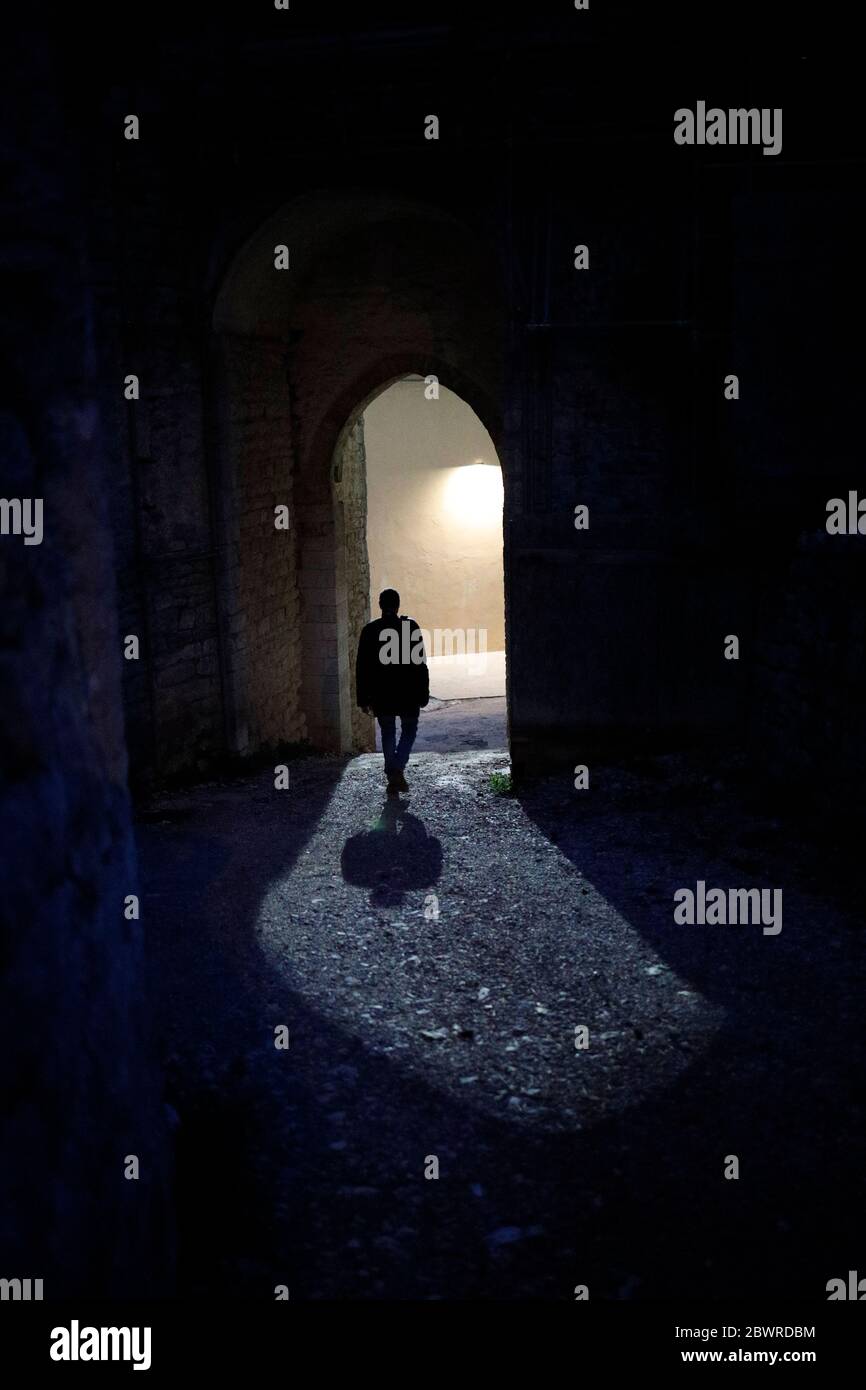Un homme vu de derrière, la nuit, marche vers une arche éclairée... Banque D'Images