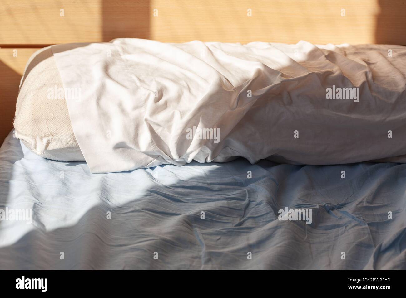 Concept de réveil : oreiller sur lit non fait avec plis sur draps éclairés par la lumière du matin Banque D'Images