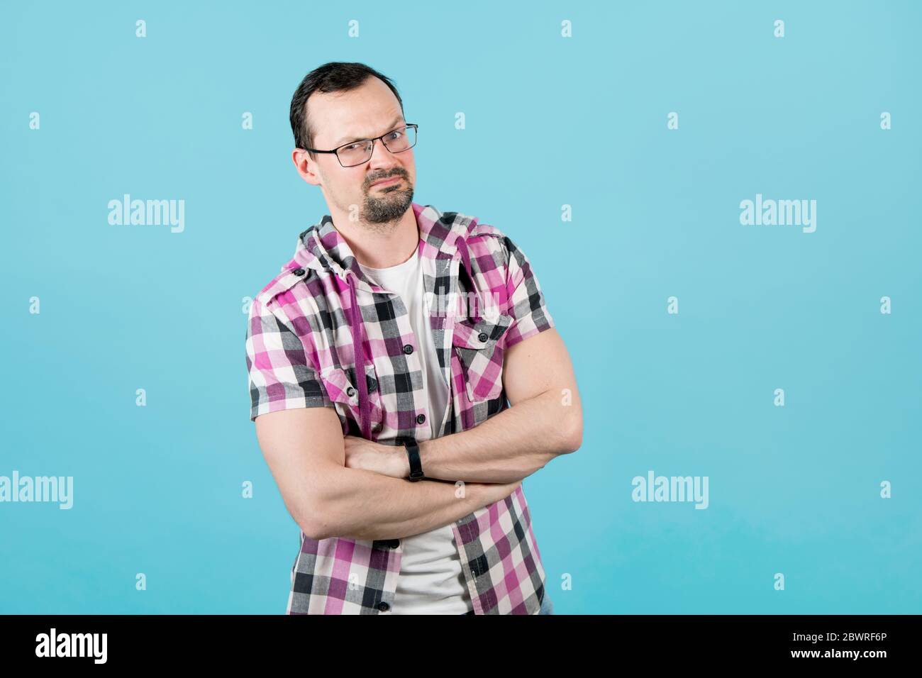 un gars avec une barbe dans une chemise de bureau a plié ses bras sur sa poitrine, une question stupide sur son visage Banque D'Images