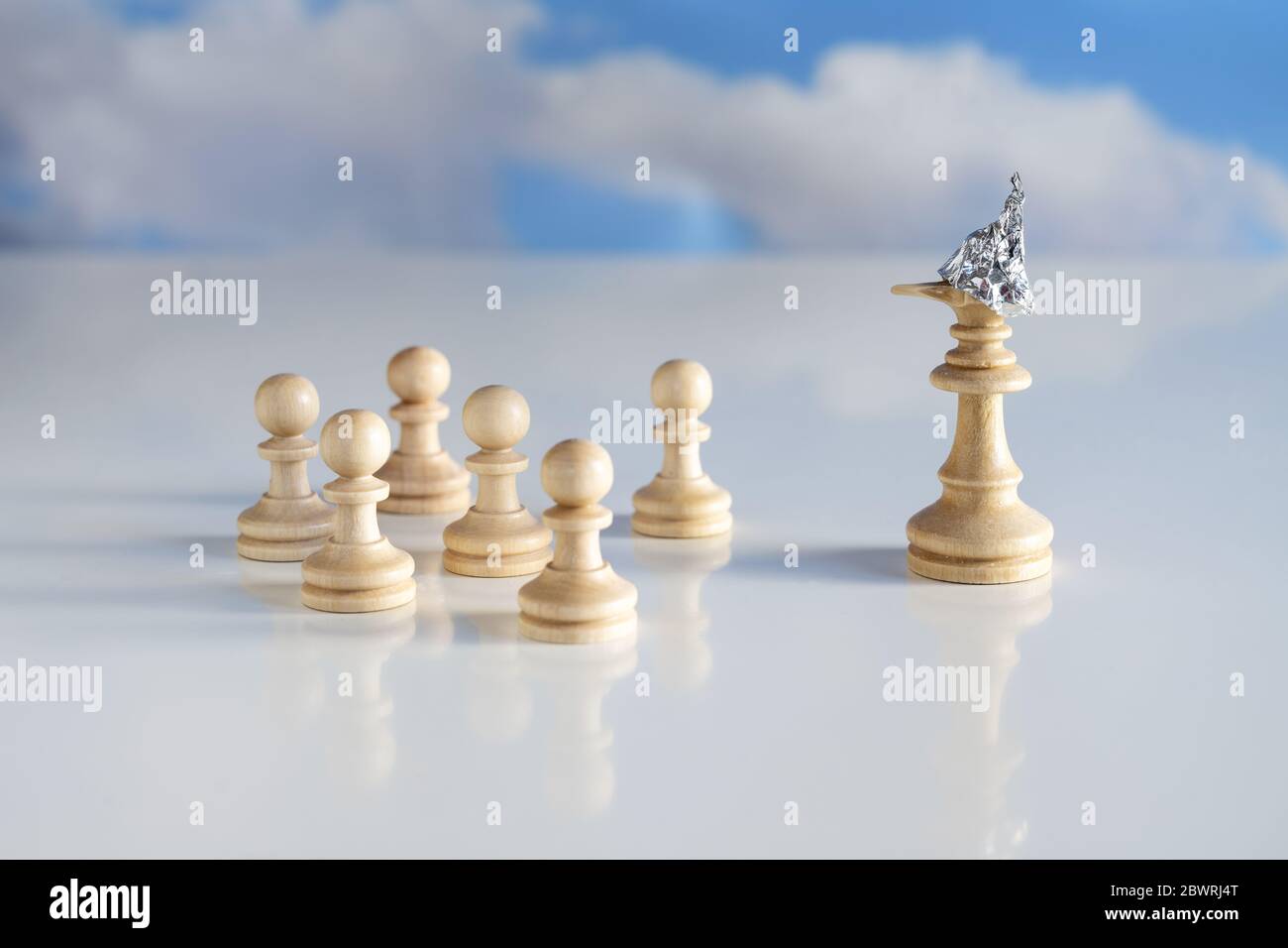 Chess morceau king ou queen avec un casque d'étain sur la tête et un long nez couché se tient devant de petites pièces de jeu, concept de la théorie de la conspiration, brig Banque D'Images