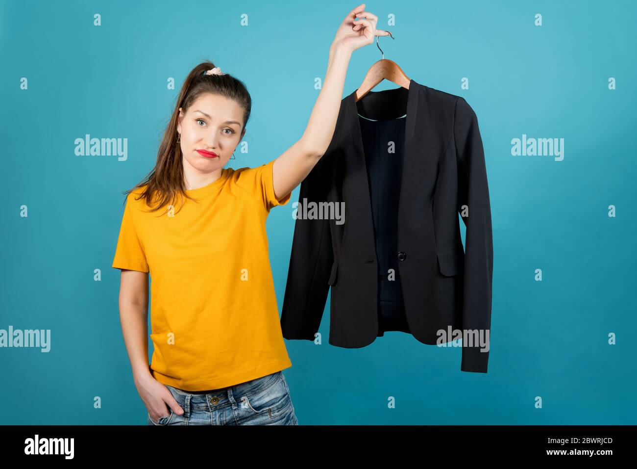 Une jeune femme en vêtements brillants avec tristesse tient dans sa main un cintre avec des vêtements de bureau stricts Banque D'Images