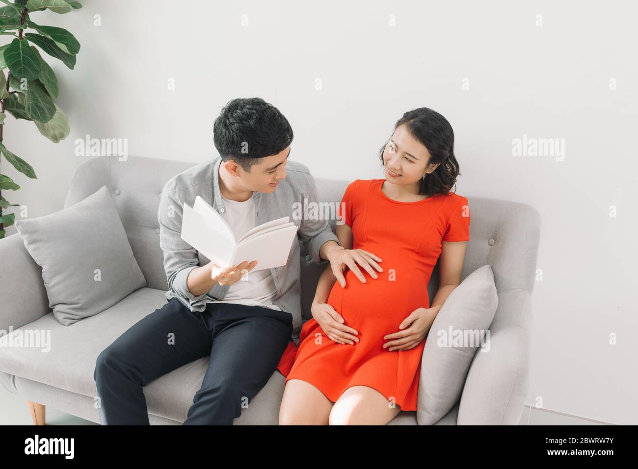 Livre de lecture de mari pour sa femme enceinte sur un canapé à la maison Banque D'Images