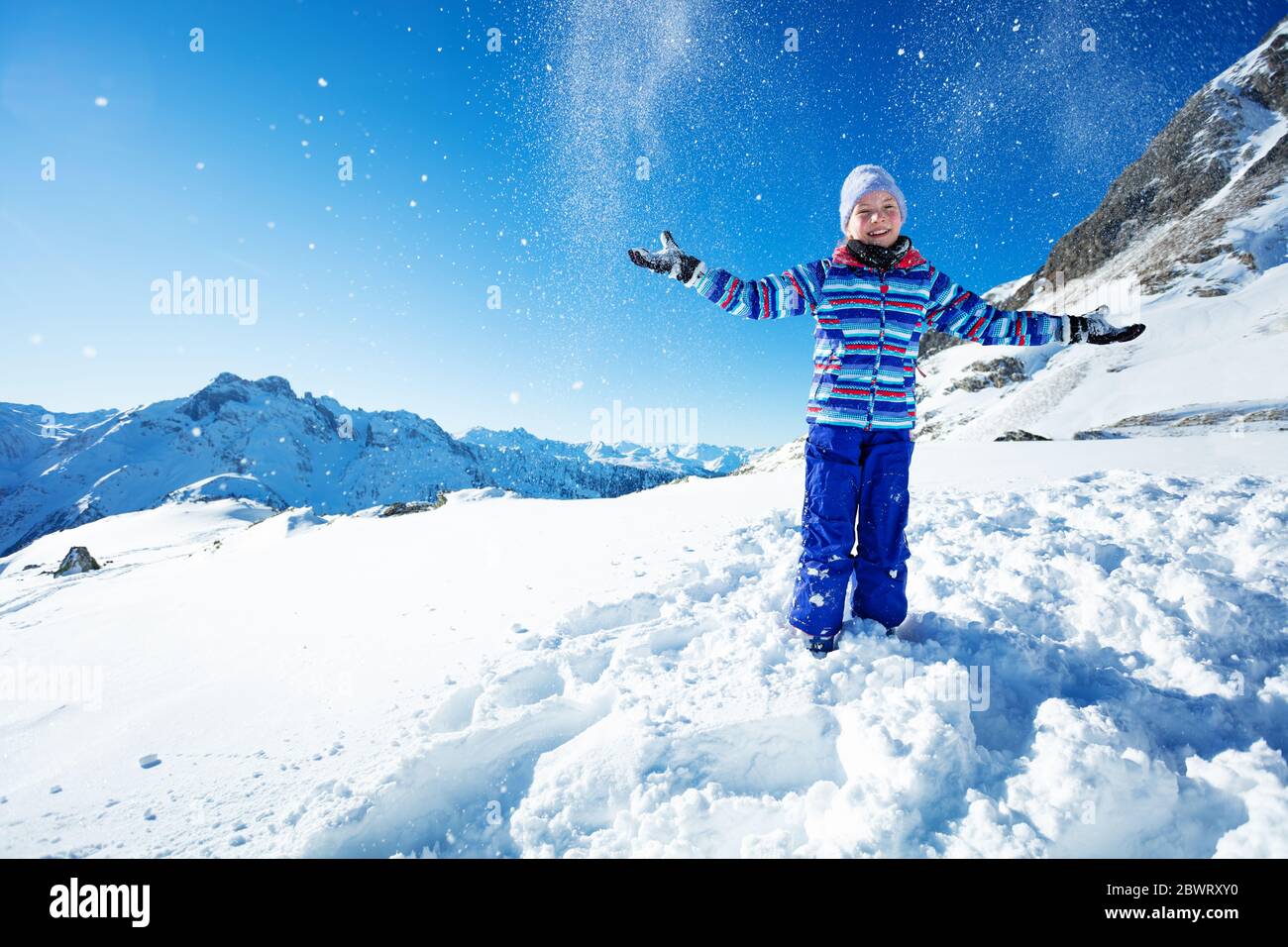 Jolie petite fille dans un ensemble de ski bleu vif jeter la neige dans l air sur la montagne et le ciel Photo Stock Alamy