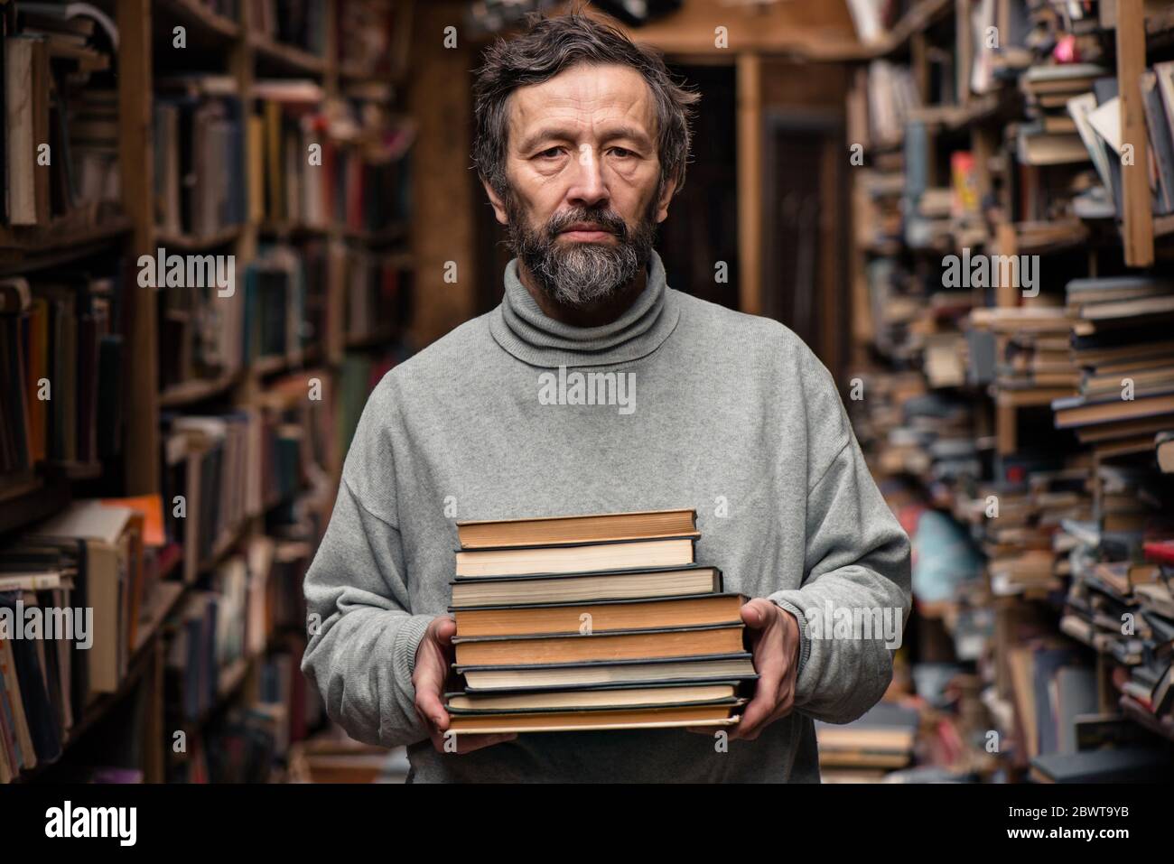 Portrait d'un homme âgé authentique avec une barbe et de bons yeux tenant des livres dans la main sur le fond du marché du livre Banque D'Images