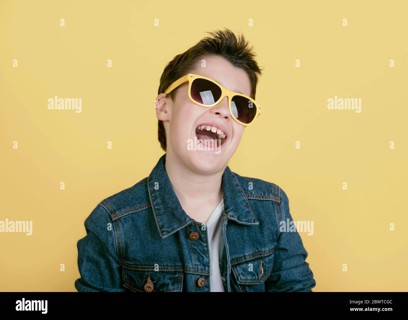 garçon souriant et heureux avec des lunettes de soleil sur fond jaune Banque D'Images