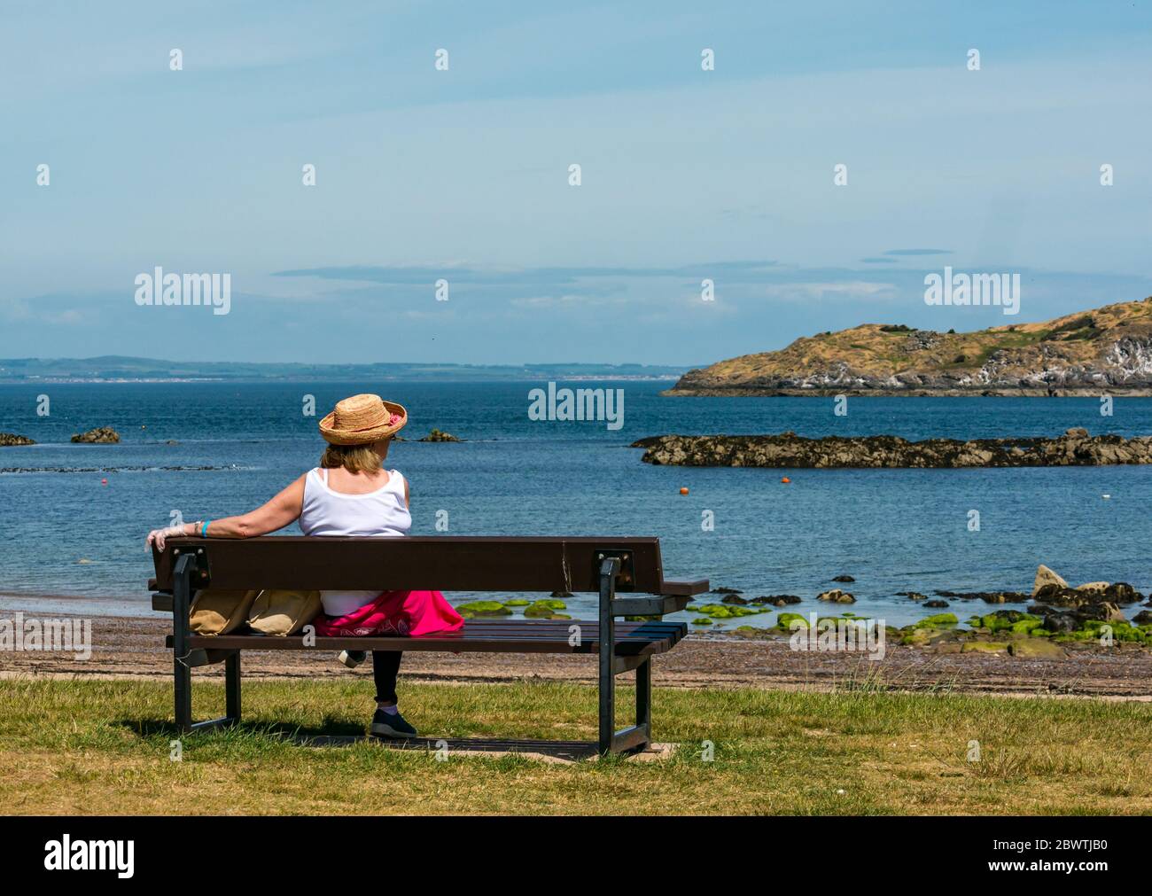 Femme portant un chapeau de paille assis sur un banc et regardant la vue le jour ensoleillé, North Berwick, Écosse, Royaume-Uni Banque D'Images