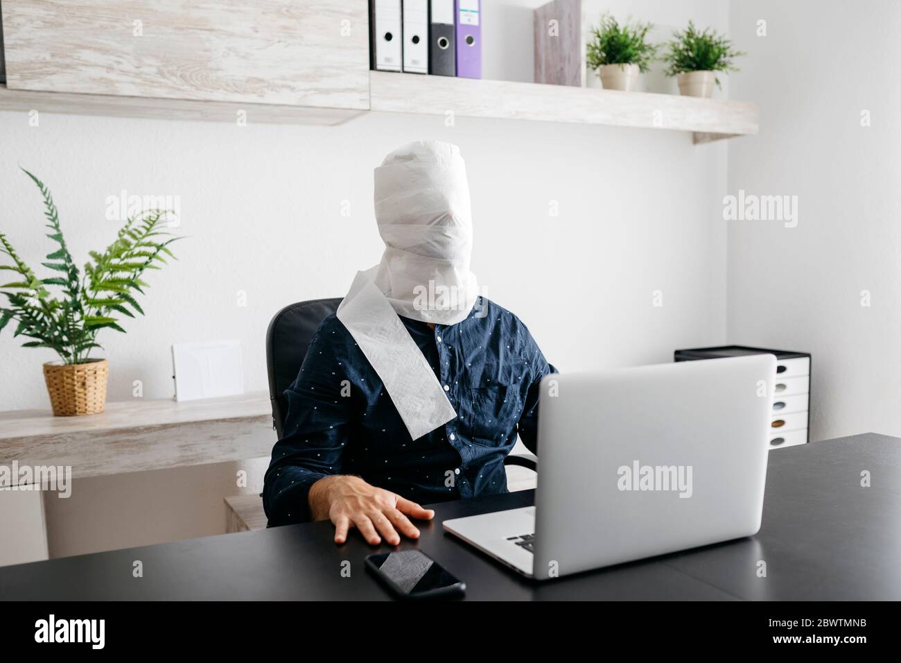 Homme travaillant à la maison avec sa tête couverte de papier toilette Banque D'Images
