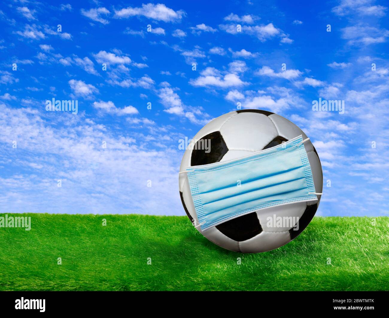 Rendu 3D, ballon de football recouvert d'un masque chirurgical sur le terrain de football Banque D'Images