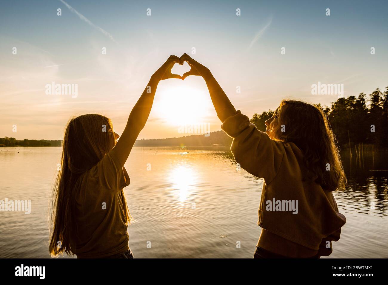 Amis qui font le coeur avec les mains contre le lac pendant le coucher du soleil Banque D'Images