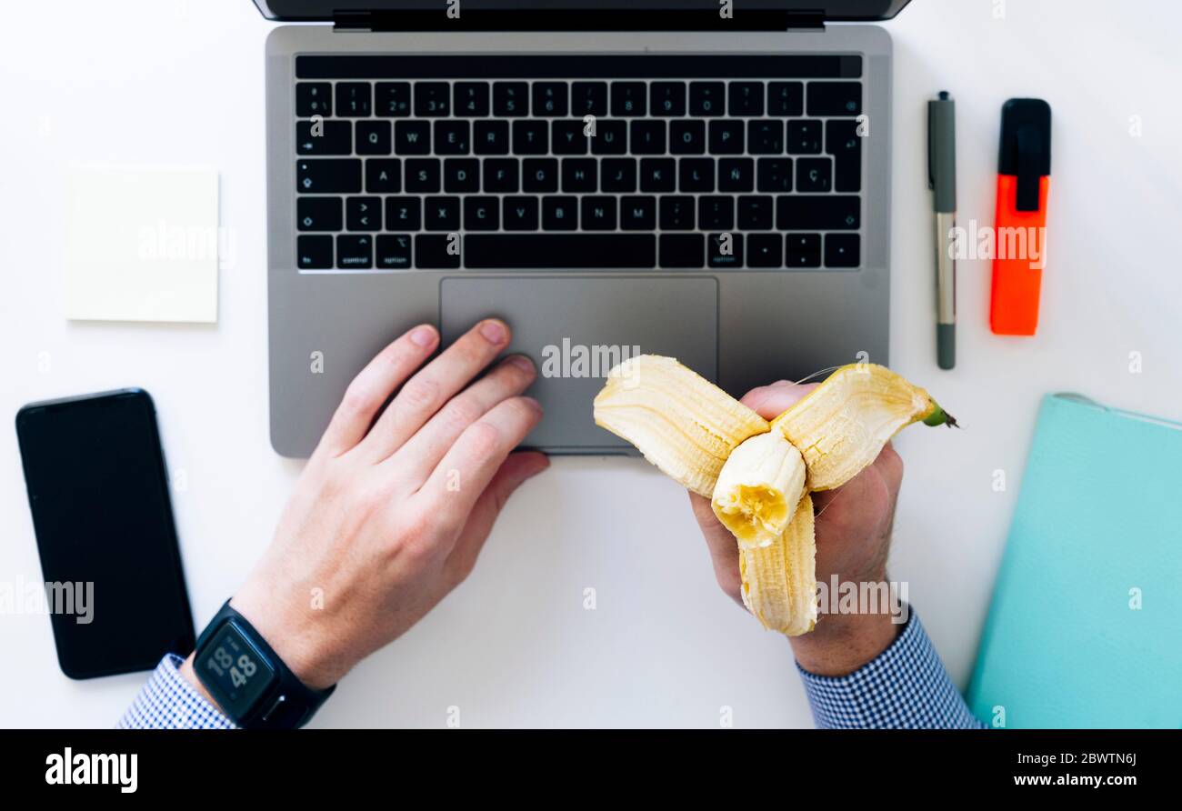 Mains de l'homme tapant sur ordinateur portable et manger de la banane Banque D'Images