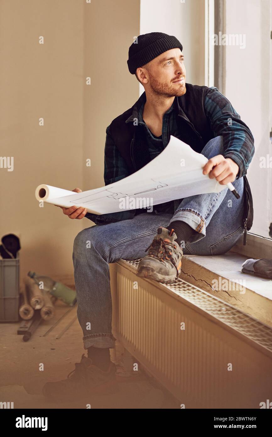 Homme en train de rénover l'atelier, assis sur le rebord de la fenêtre, étudiant le plan Banque D'Images
