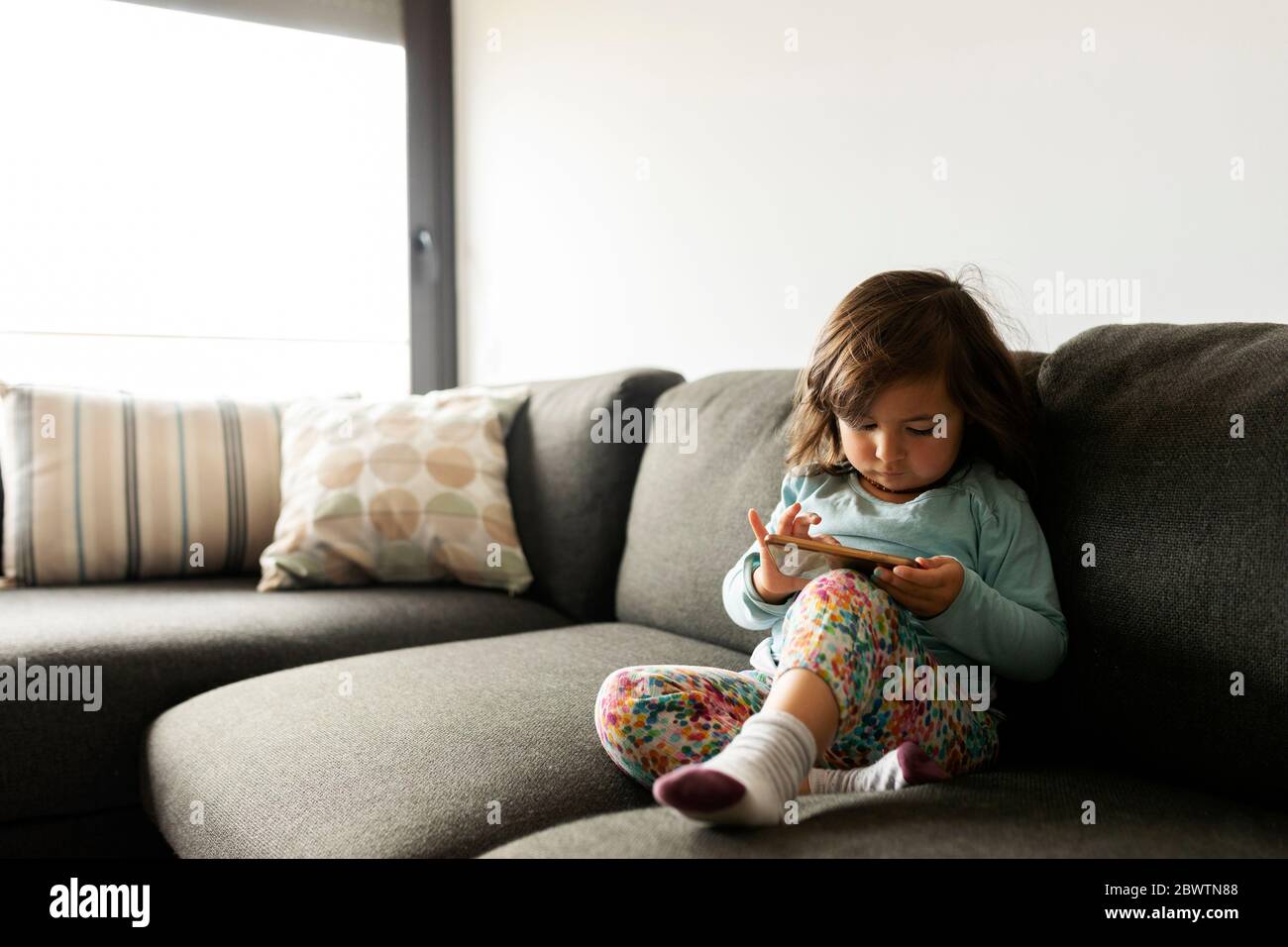 Petite fille assise sur un canapé à la maison à l'aide d'un smartphone Banque D'Images