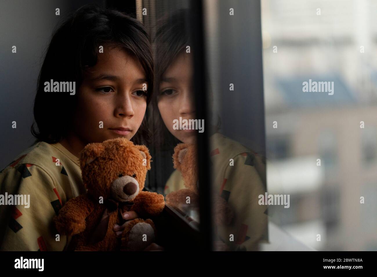 Garçon avec son ours en peluche regardant par la fenêtre à la maison Banque D'Images