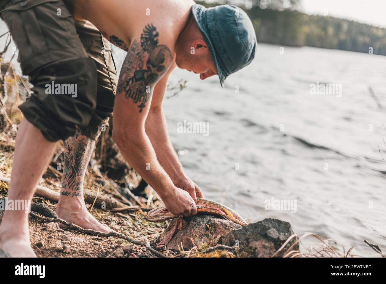 Un jeune homme évisse des poissons sur le bord du lac Banque D'Images