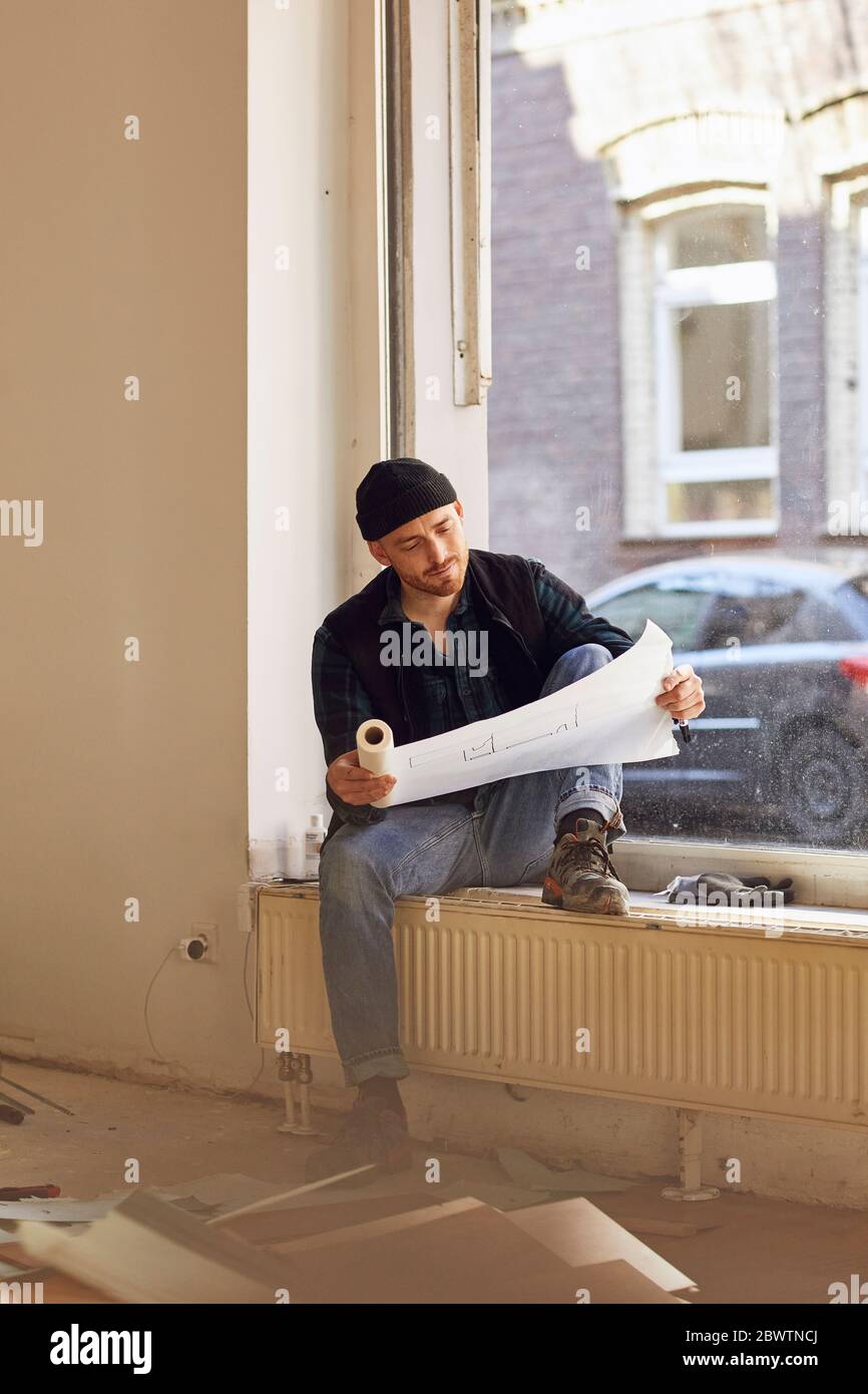 Homme en train de rénover l'atelier, assis sur le rebord de la fenêtre, étudiant le plan Banque D'Images