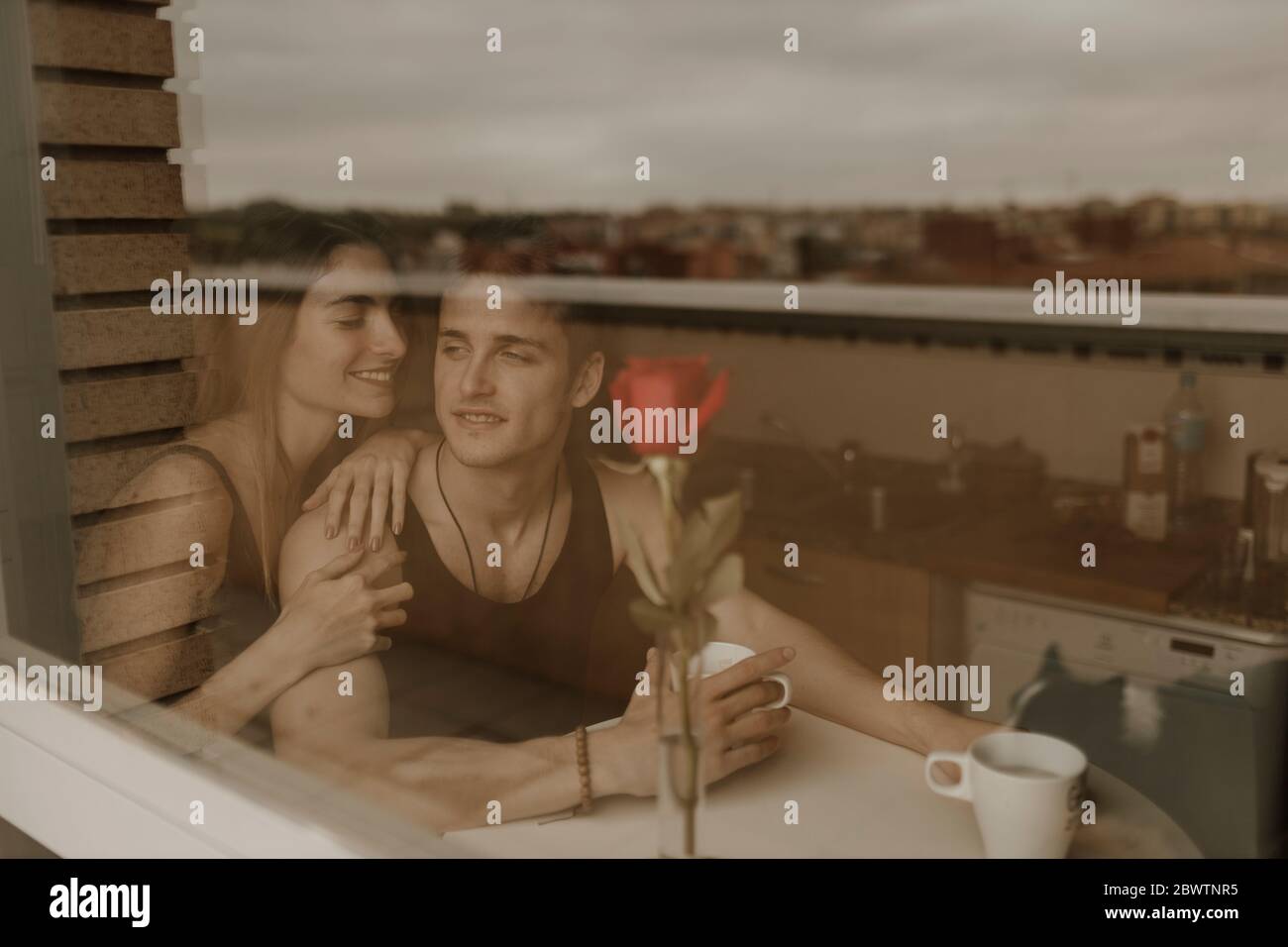 Jeune couple romantique avec rose rouge derrière le panneau de fenêtre Banque D'Images
