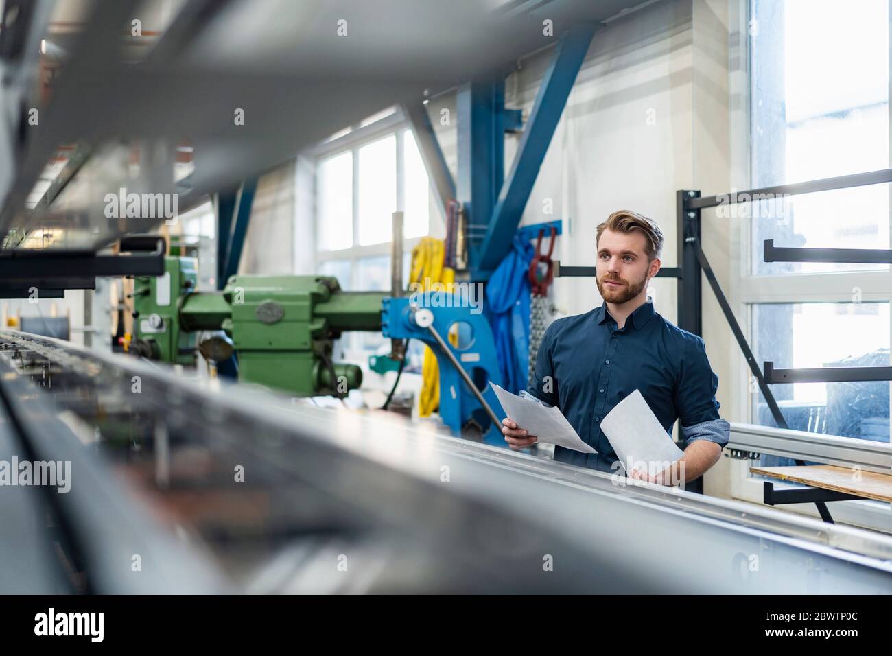 Jeune homme tenant des papiers dans une usine Banque D'Images