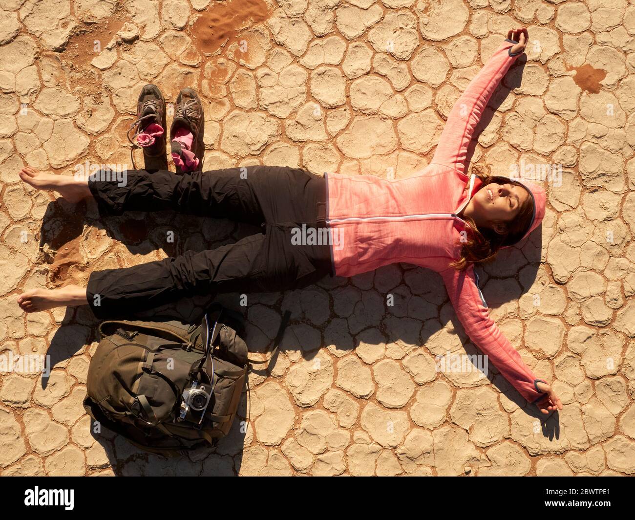 Femme pieds nus et son sac à dos allongé sur le plancher sec de la casserole craqué à Deadvlei, Namibie. Banque D'Images