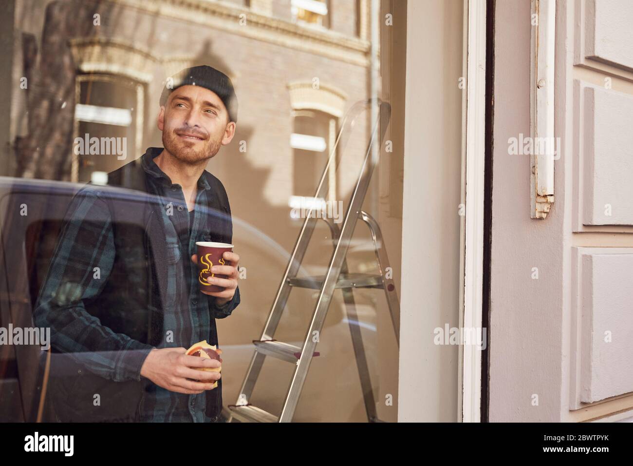 Homme rénolisant l'emplacement de l'atelier, prenant du café, regardant par la fenêtre Banque D'Images