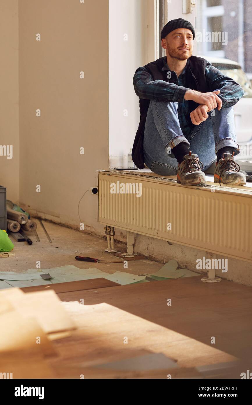 Homme en train de rénover l'atelier, assis sur le rebord de la fenêtre Banque D'Images