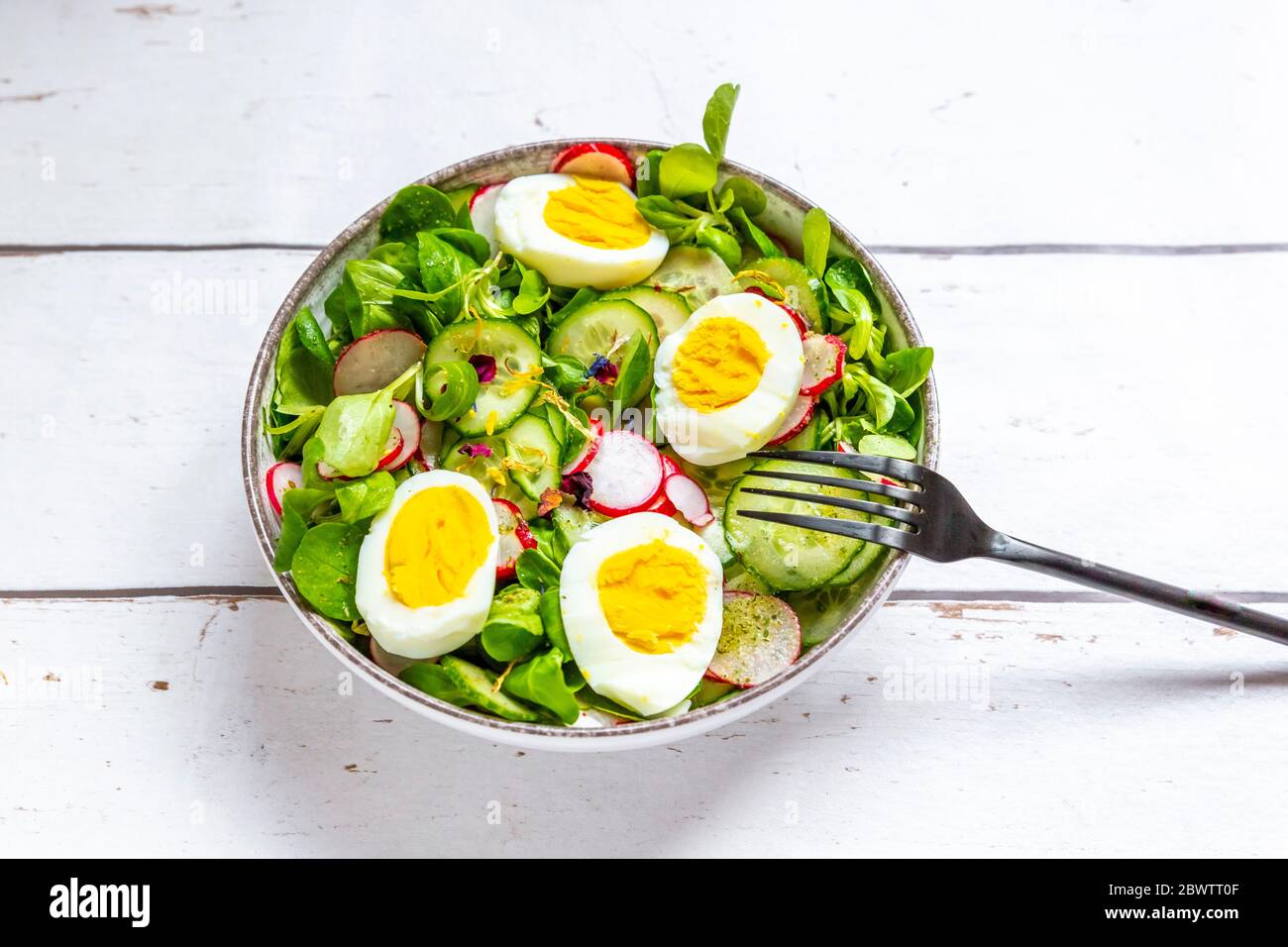 Bol de salade végétarienne avec œufs durs, radis, concombres, salade de maïs et fleurs comestibles Banque D'Images