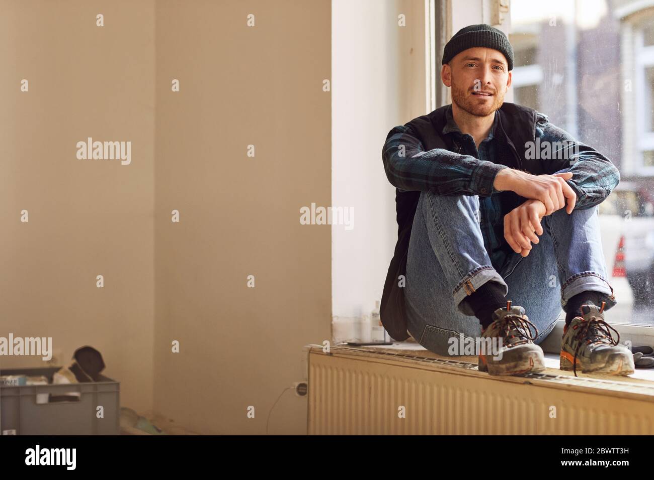 Homme en train de rénover l'atelier, assis sur le rebord de la fenêtre Banque D'Images