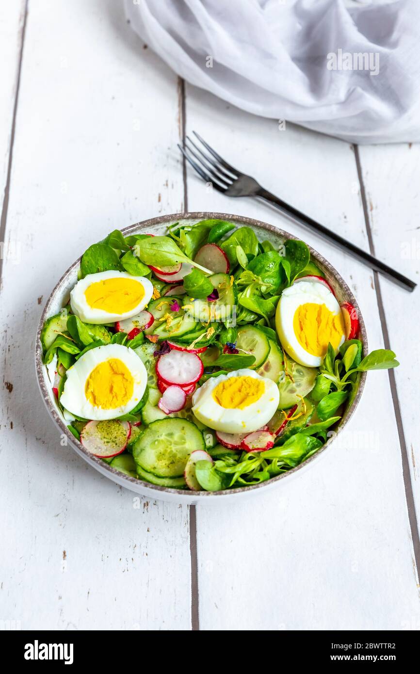 Bol de salade végétarienne avec œufs durs, radis, concombres, salade de maïs et fleurs comestibles Banque D'Images