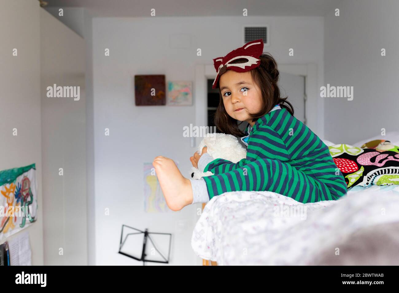 Portrait de petite fille avec masque de renard assis sur un lit superposé pieds nus à la maison Banque D'Images