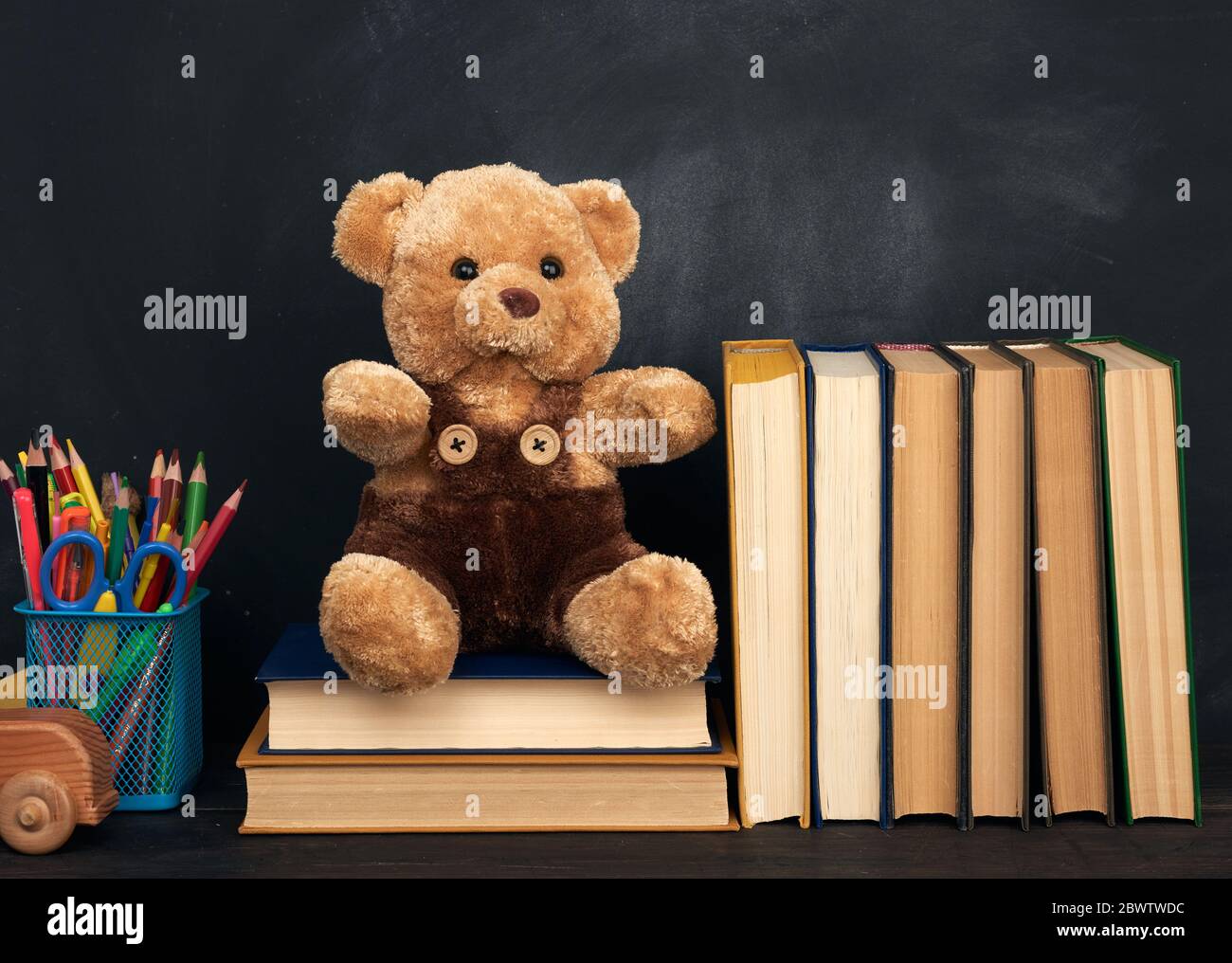 l'ours en peluche brun est assis sur une table en bois brun, derrière un tableau noir vide, pour rentrer à l'école Banque D'Images