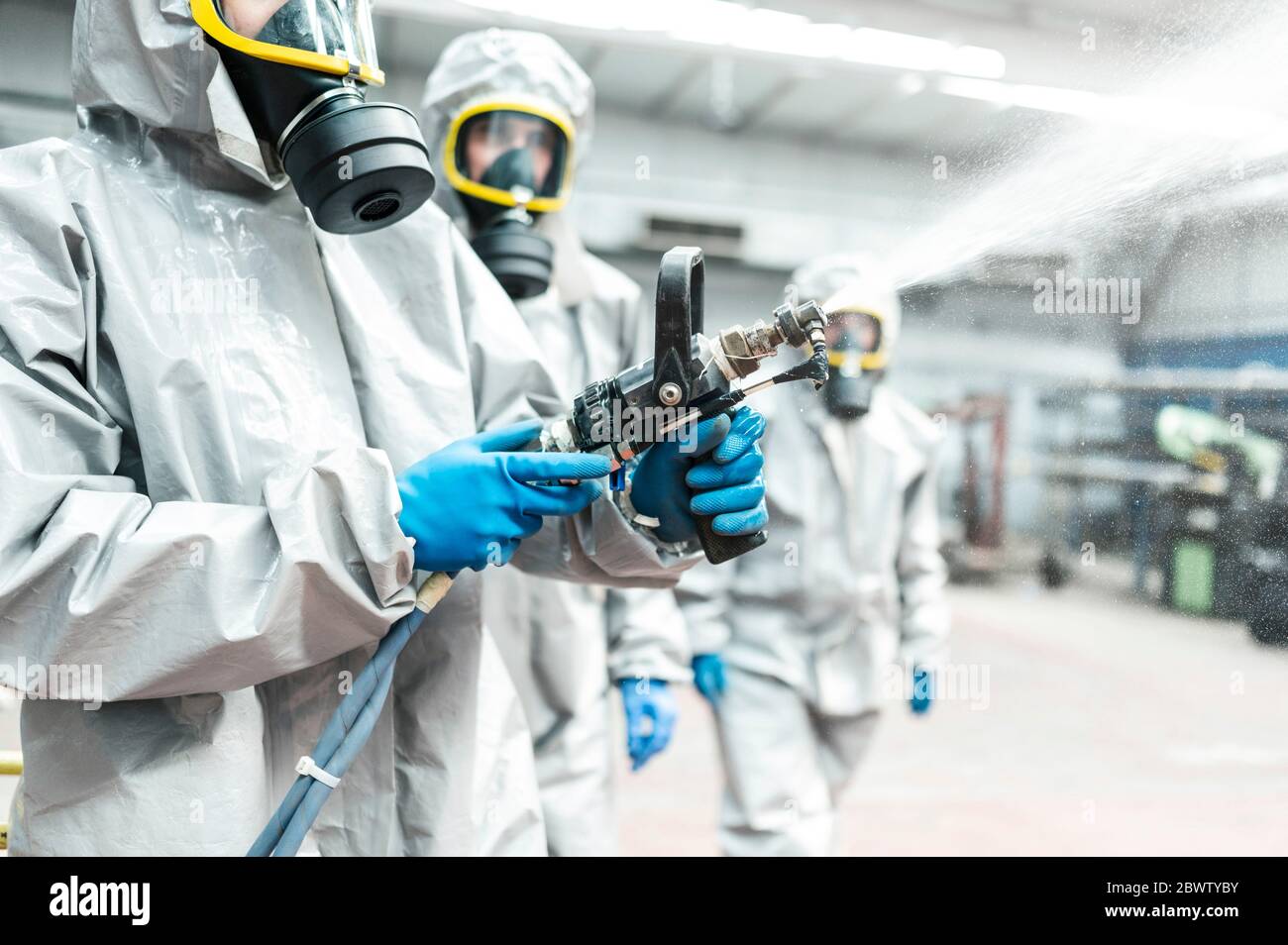 Un travailleur sanitaire pulvérisant du produit chimique de décontamination à partir d'un tuyau Banque D'Images