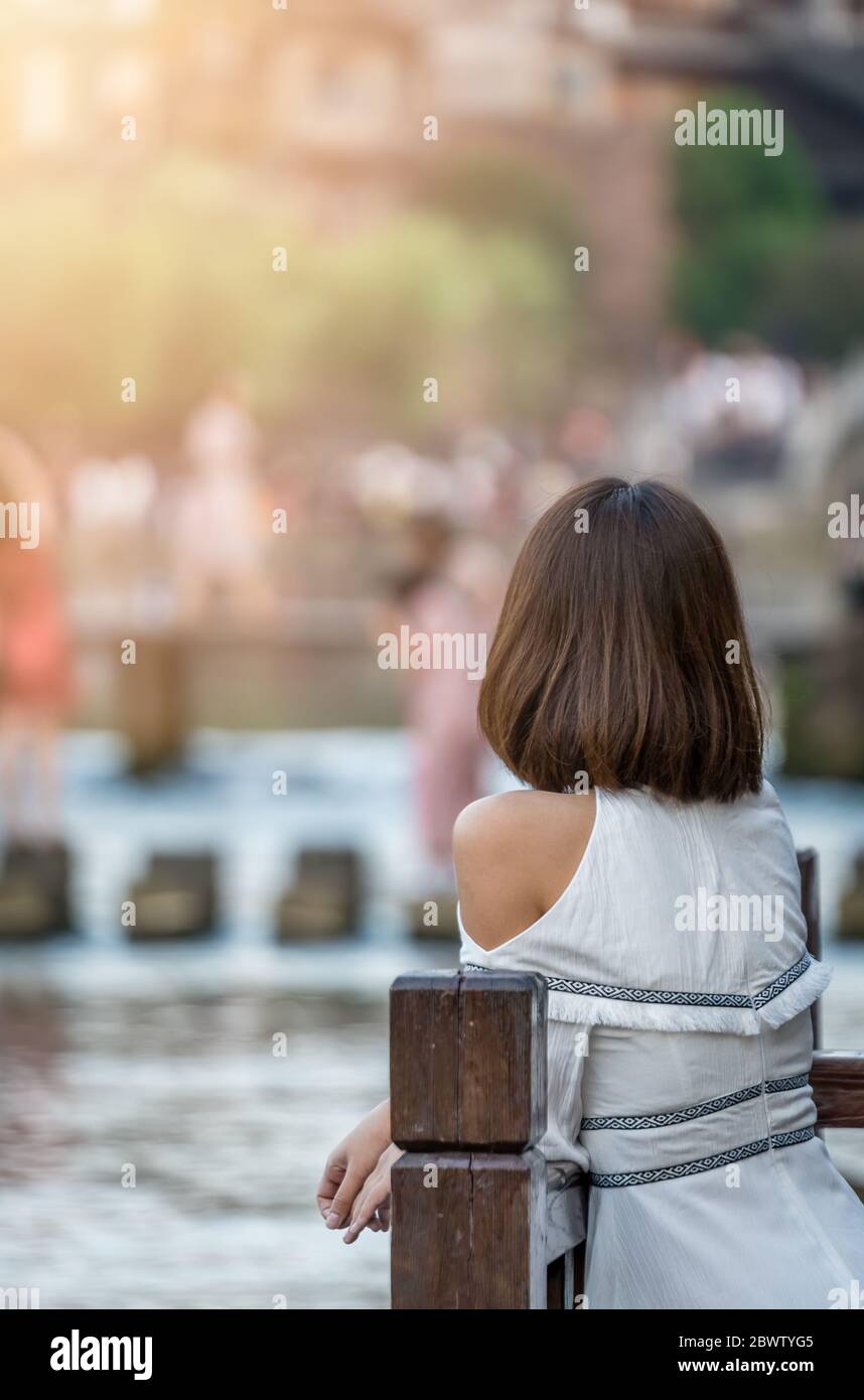 Feng Huang, Chine - août 2019 : belle jeune chinoise habillée de robe blanche penchée sur la barrière en bois et posant pour une photo sur le TH Banque D'Images