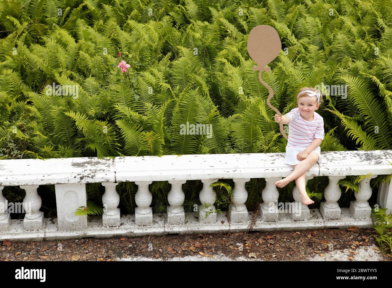 Petite fille assise sur une balustrade tenant un ballon en carton Banque D'Images