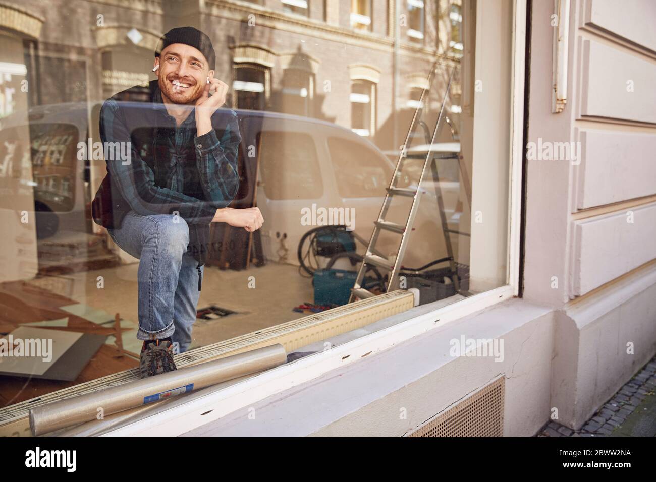 Homme rénolisant l'atelier, en utilisant des écouteurs à la fenêtre Banque D'Images