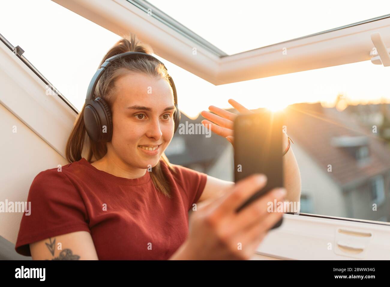 Jeune femme ayant un chat vidéo à la fenêtre en contre-jour Banque D'Images