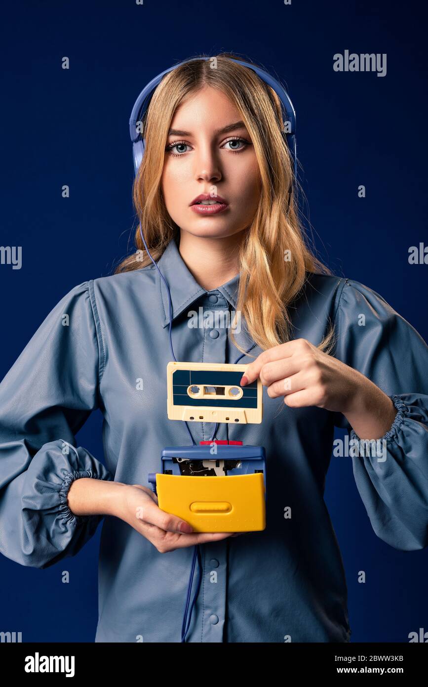 Jeune femme blonde avec walkman et écouteurs devant un fond bleu Banque D'Images