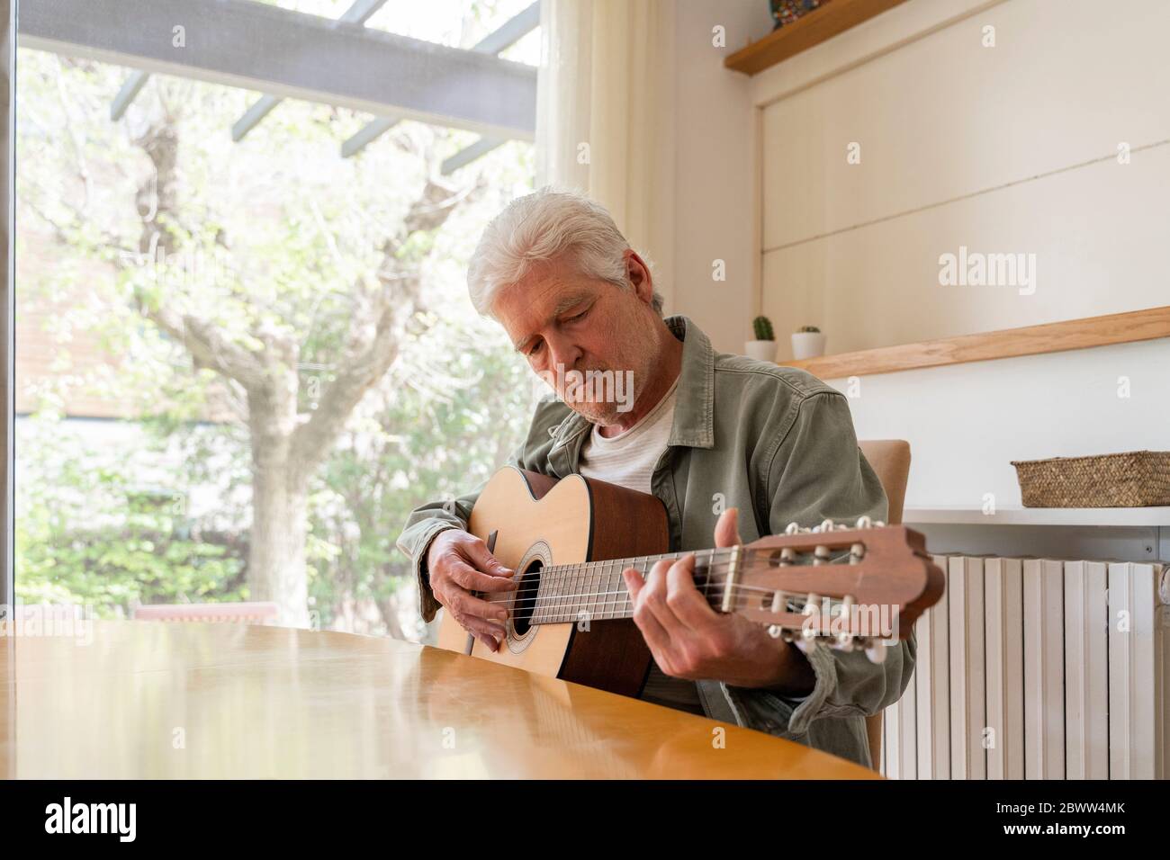 Homme âgé qui plage des cordes de guitare tout en pratiquant à la maison Banque D'Images