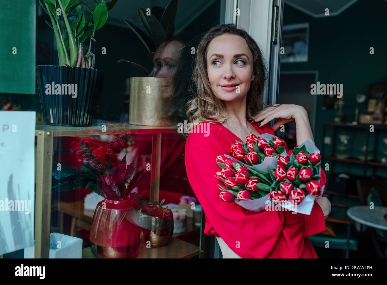 Femme souriante avec un bouquet de fleurs à la fenêtre dans un fleuriste Banque D'Images