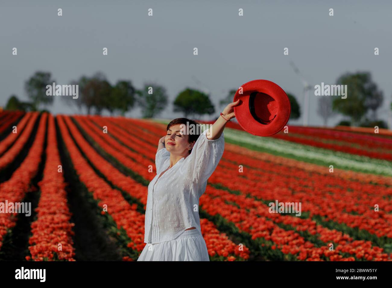 Portrait d'une femme souriante avec un chapeau rouge debout devant le champ de tulipe Banque D'Images