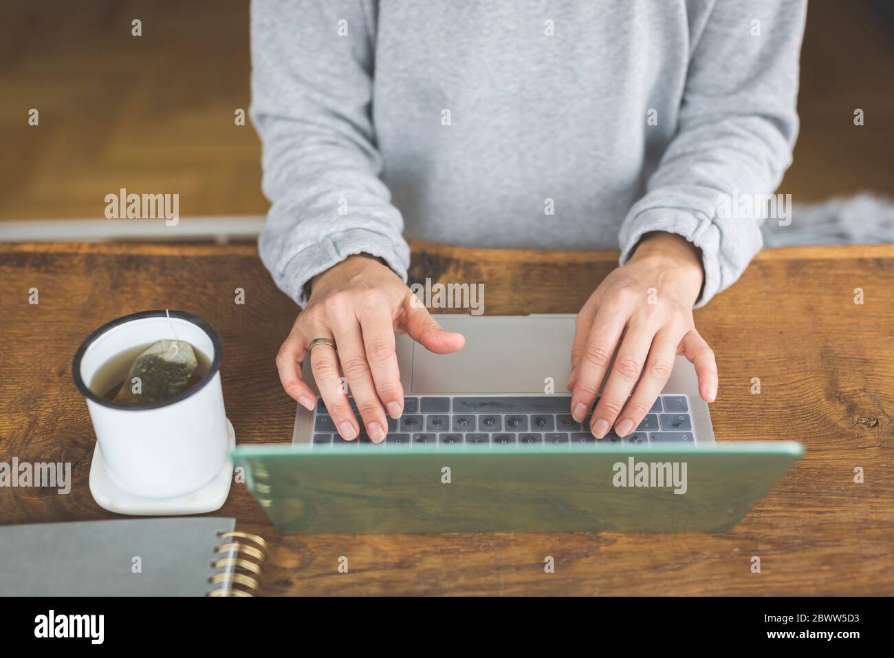 Femme travaillant sur un ordinateur portable, avec une tasse de thé sur le côté Banque D'Images