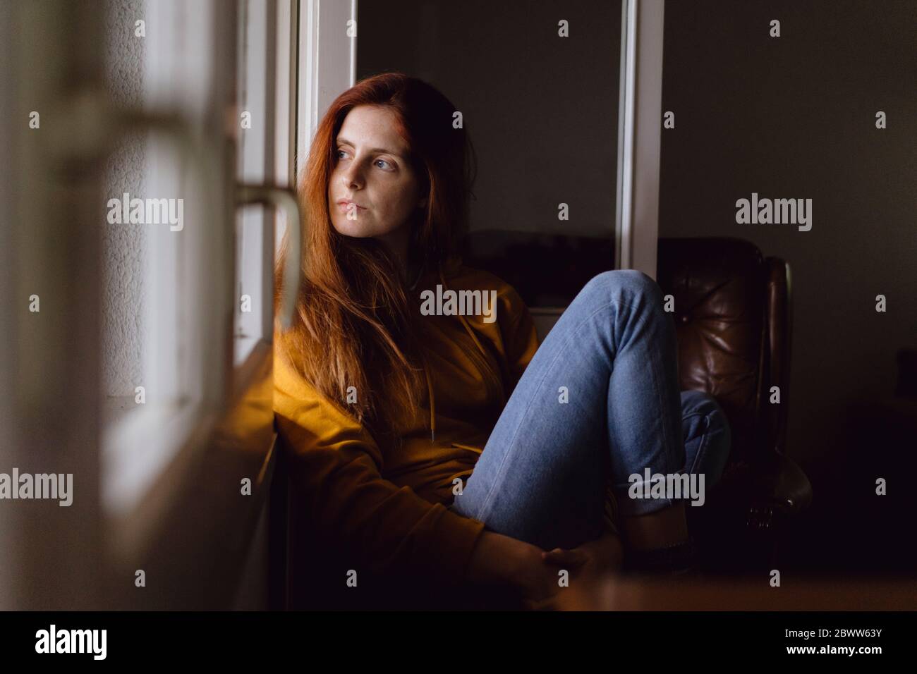 Portrait d'une femme à tête rouge assis à une fenêtre ouverte regardant la maison à distance Banque D'Images