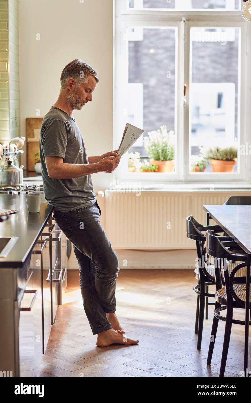 Homme mature lisant le journal dans la cuisine à la maison Banque D'Images