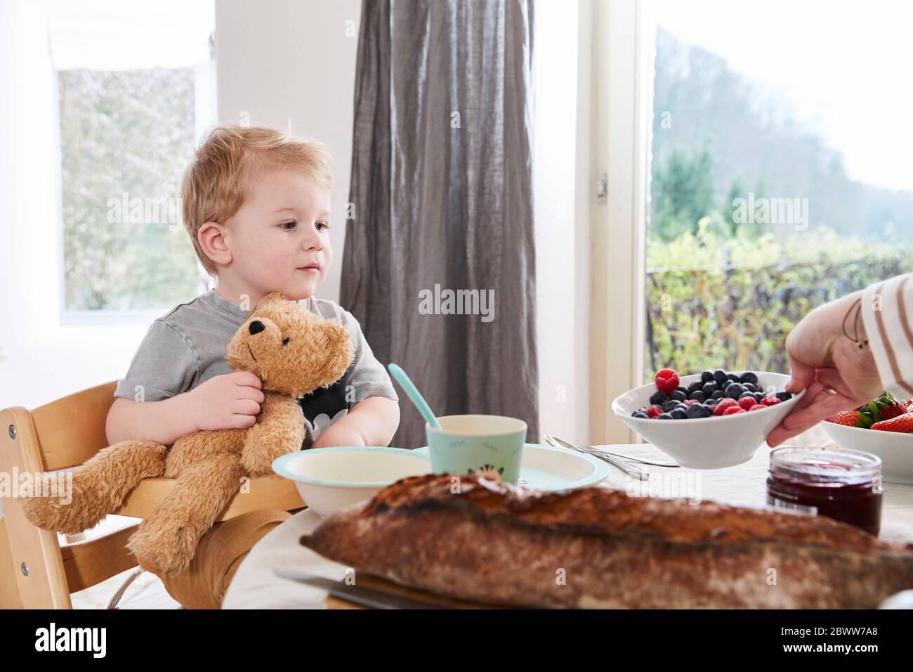 Portrait d'un petit garçon assis à la table du petit déjeuner avec un ours en peluche Banque D'Images