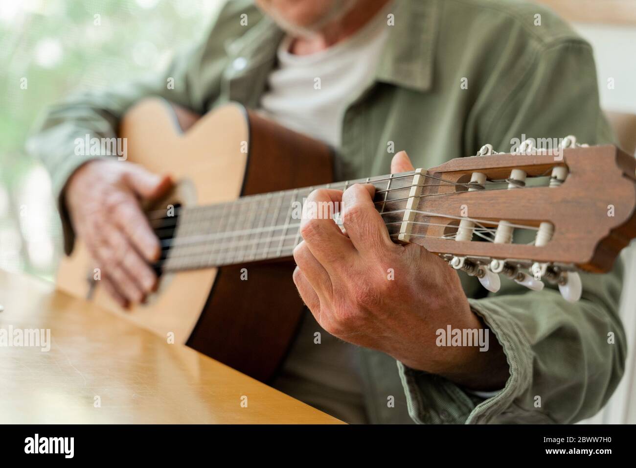 Mi-section de l'homme retraité pratiquant la guitare tout en étant assis à la maison Banque D'Images