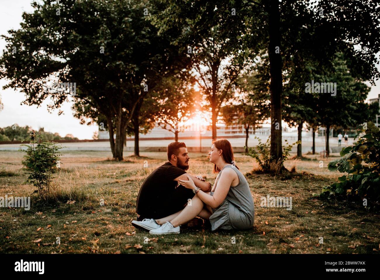 Jeune couple assis dans un parc au coucher du soleil Banque D'Images