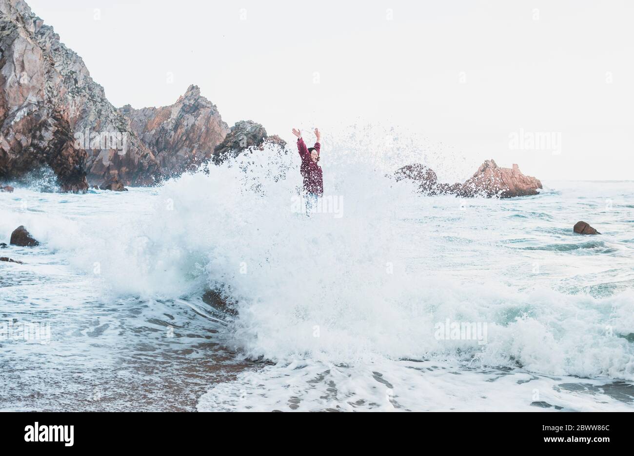 Jeune femme debout sur le rocher avec une grande vague, Praia da Ursa, Lisboa, Portugal Banque D'Images